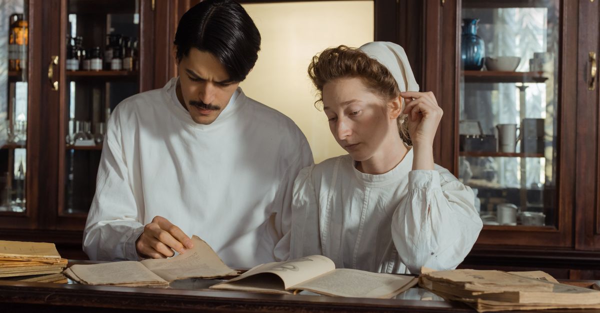 Two pharmacists in vintage attire examining old pharmaceutical texts in a historical pharmacy.